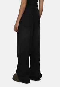 Zwarte denim jeans met wijde benen en een hoge taille, met twee achterzakken, zichtbare stiksels en een gladde textuur.