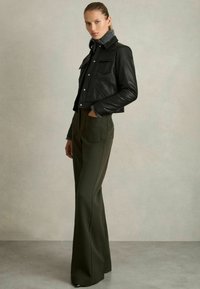 Schwarze Leder-Bikerjacke mit silbernen Details, grauem Kragen, kombiniert mit hoch taillierten olivgrünen Hosen mit seitlichen Taschen.