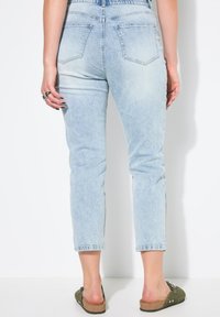 Jeans de mezclilla de color azul claro, de talle alto y ajuste ceñido, con bolsillos traseros y dobladillos ligeramente deshilachados, combinados con zuecos verdes.