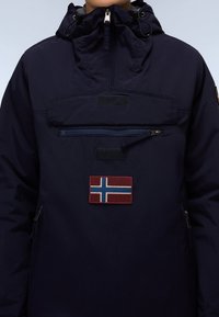 Navy blue jacket with a high collar, front zip pocket, and Norway flag patch. Features drawstrings and smooth, textured fabric.