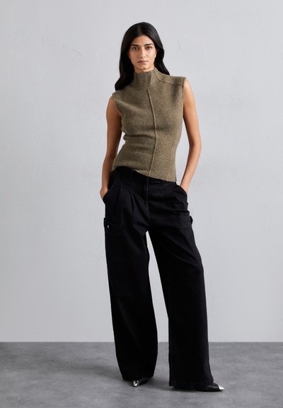 Olivgrünes ärmelloses Stricktop mit hohem Kragen, kombiniert mit lockeren schwarzen Cargo-Hosen mit Taschen und einer entspannten Passform.