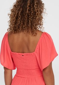 Koralfärgad klänning med fyrkantig halsringning, smockad bodice och puffärmar. Tyget har ett mjukt, texturerat utseende.