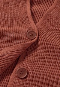 Gerecceerde ribkaarten in roestkleur, met twee ronde bruine knopen en een zachte, gebreide stof, die een casual ontwerp tentoonstelt.