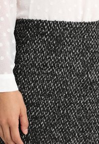 Zavinovací sukně v černobílém vzoru s texturovanou tkaninou. Obsahuje přiléhavý pas. Částečně viditelná bílá halenka s puntíky.
