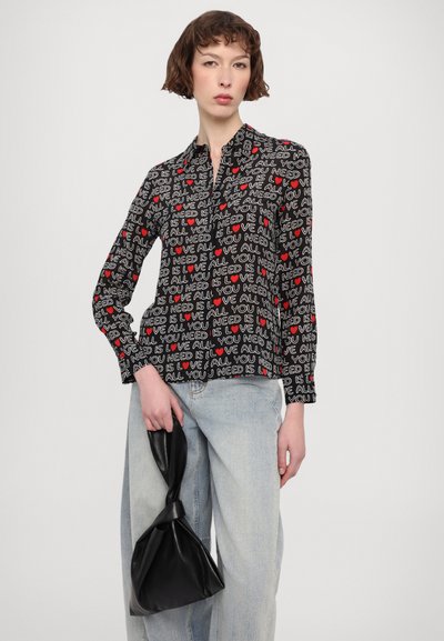 Black button-up shirt featuring a repetitive text and heart print in red and white. Paired with light blue denim and a black knotted bag.