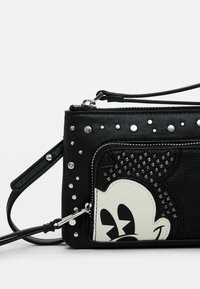 Bolso de piel negra cruzado con acentos de tachuelas, un compartimento con cremallera y un gráfico de un personaje de dibujos animados en la parte delantera.