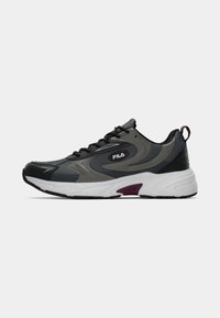 Sneakers marki Fila w czerni, szarości i bieli; charakteryzują się teksturowaną cholewką, zakrzywionym kształtem oraz fioletowymi akcentami na pięcie i logo.