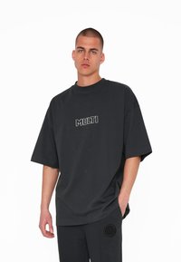 Sort oversized t-shirt lavet af bomuld, med en rund halsudskæring og et hvidt broderet "MULTI" logo på brystet.