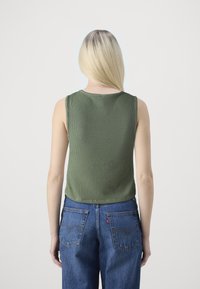 Green ribbed tank top with a round neckline, paired with blue denim jeans featuring back pockets and a visible brand tag.