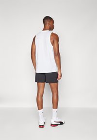 Mannelijke sportoutfit met een witte mouwloze tanktop, zwarte shorts, witte sokken en sportschoenen met rode accenten.
