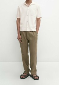 Kortlopende, lichtroze shirt met een borstzak, gecombineerd met losse, olijfgroene broek en zwarte sandalen. Eenvoudig ontwerp en neutrale kleuren.