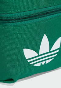 Zöld szövet táska texturált felülettel, fehér Adidas logóval és csíkokkal. A dizájn cipzáras z�áródást tartalmaz.