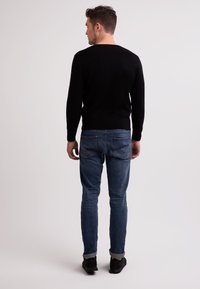 Maglione nero con maniche lunghe e scollatura a girocollo, abbinato a jeans blu con vestibilità classica e risvolto. Calzature nere completano il look.