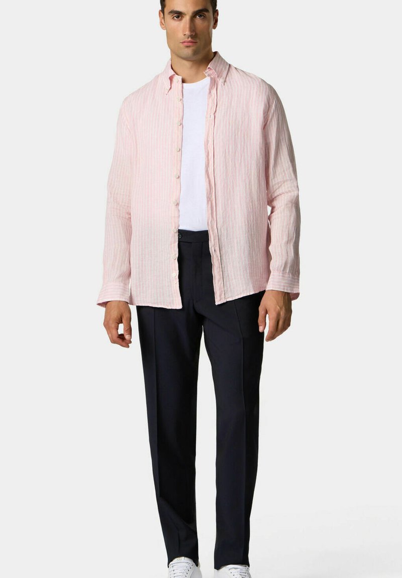 Camicia di lino a righe rosa chiaro con maniche lunghe e chiusura a bottoni, indossata sopra una maglietta bianca e abbinata a pantaloni scuri e sneakers bianche.