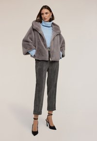 Szara kurtka z sztucznego futra z kapturem, z zapięciem na zamek, w połączeniu z jasnoniebieskim swetrem dzianinowym i szarymi spodniami z korduroy. Czarne buty na obcasie dopełniają zestaw.