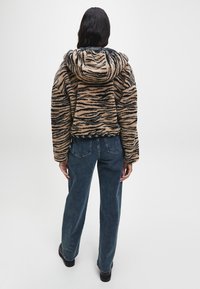 Kaptur z futra syntetycznego w wzór tygrysa w odcieniach beżu i czerni, z kapturem ze sznurkiem i prążkowanym wykończeniem, połączony z dżinsami o szerokich nogawkach.
