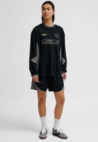 Zwart longsleeve shirt met ribbelstructuur en grijze accenten, gecombineerd met zwarte shorts. Voorzien van een gouden logo en merknaam.