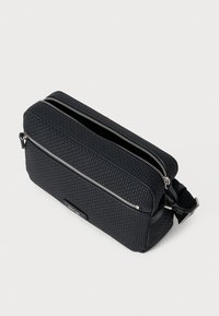 Μαύρη ορθογώνια τσάντα κατασκευασμένη από υλικό με υφή, με δύο ασημένιες θήκες με φερμουάρ και αποσπώμενη θήκη για μεταφορά.