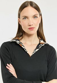 Camicia nera a maniche lunghe con un colletto vivace a motivo, caratterizzato da righe e accenti solidi. Tessuto morbido, vestibilità comoda con scollatura a V.