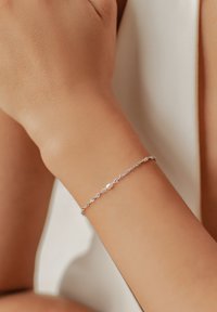 Pulsera de plata con un diseño retorcido, que presenta un único acento de perla. Usada en una muñeca, mostrando un tono de piel suave y claro.