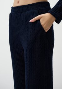 Navy blue knitted pants feature a textured surface, side pockets, and an elastic waistband for a comfortable fit.