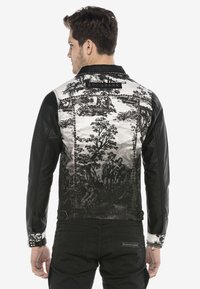 Schwarze Lederjacke mit einem detaillierten silber- und schwarzbedruckten Rückendesign, das Szenen aus der Natur und Figuren zeigt, sowie Nietenakzenten entlang der Nähte.