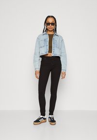 Denim cropped jakke i lys blå, svarte skinny jeans, svarte sneakers med hvite detaljer og rektangulære solbriller.