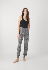 Débardeur noir associé à un pantalon ample à motif noir et blanc. Les pantalons ont des poignets élastiques et des poches latérales.