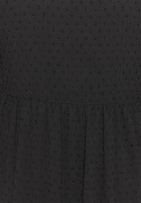 Černé šaty z texturované tkaniny s vyvýšeným tečkovaným vzorem, s nabíranou sukní a hladkým tělem.