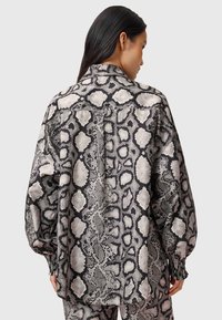 Blusa a maniche lunghe in stampa serpente, con una combinazione di squame nere, bianche e grigie. Realizzata in un tessuto morbido con una vestibilità comoda e maniche regolabili.