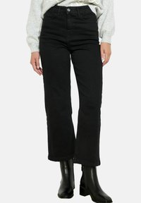 Mustmustest kõrge vöökohtadega mustad denim teksad sirge säärtega, veidi kulunud äärega, kaasas heledhalli kampsuni ja mustade pahkluu saapadega.