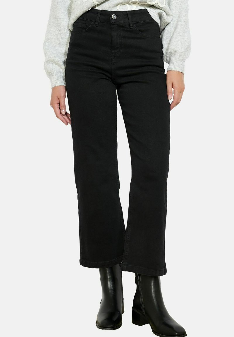 Mustmustest kõrge vöökohtadega mustad denim teksad sirge säärtega, veidi kulunud äärega, kaasas heledhalli kampsuni ja mustade pahkluu saapadega.