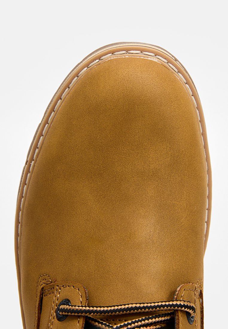 Bruine leren boot met een gladde textuur, ronde neus, contrasterend witte stiksels en zwarte veters die door metalen oogjes zijn geregen.