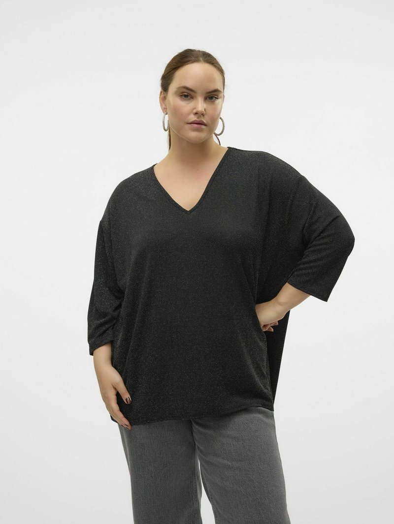 Tunique noire à col en V avec des manches courtes et larges, présentant un léger scintillement et une coupe ample. Associée avec un pantalon gris texturé.