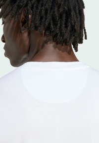 Bílý triko s kulatým výstřihem a krátkými rukávy, s hladkou texturou a viditelným švem podél límce.