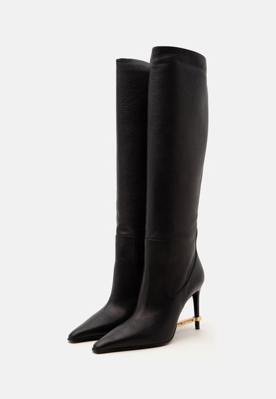 Paire de bottes hautes en cuir noir à bout pointu avec des talons hauts et fins ornés d'accents de barre horizontale dorée.