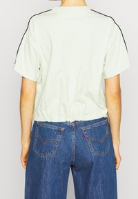 Camiseta de algodón verde claro con un diseño corto y rayas negras a los lados, combinada con unos pantalones vaqueros de mezclilla oscuros de tiro alto que tienen dos bolsillos en la parte posterior.