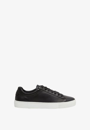 Schwarzer flacher Ledersneaker mit schwarzen Schnürsenkeln und weißer Gummisohle, von der Seite auf weißem Hintergrund gezeigt.