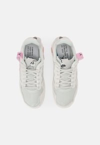 Paire de baskets Nike Air gris clair avec lacets blancs, petites languettes roses ornées de logos Jumpman, et texte imprimé à l'intérieur des colliers de chaussures.