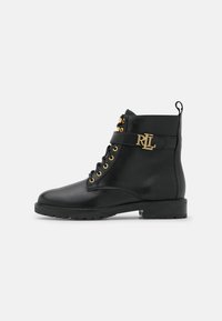 Botas de piel negra hasta el tobillo con ojales dorados y una correa decorativa que presenta el monograma. Suela gruesa y tirador para facilitar su uso.