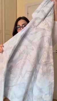 Femme portant des lunettes tenant un grand tissu de couleur claire avec des motifs abstraits subtils à l'intérieur.