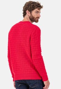 Pull rouge tricoté avec un motif en relief style panier et des poignets et un ourlet côtelés. Il présente un col rond et des manches longues.