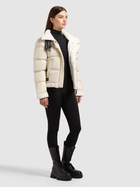 Kurtka puchowa w jasnobeżowym kolorze z kołnierzem z baranka, czarnymi akcentami i kieszeniami na zamek. W połączeniu z czarnymi legginsami i sznurowanymi botkami bojówkami.