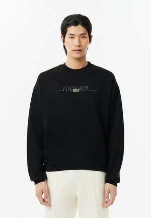 Black sweatshirt made of cotton blend, featuring a round neck, long sleeves, and 'LACOSTE' embroidered logo in green on the front.