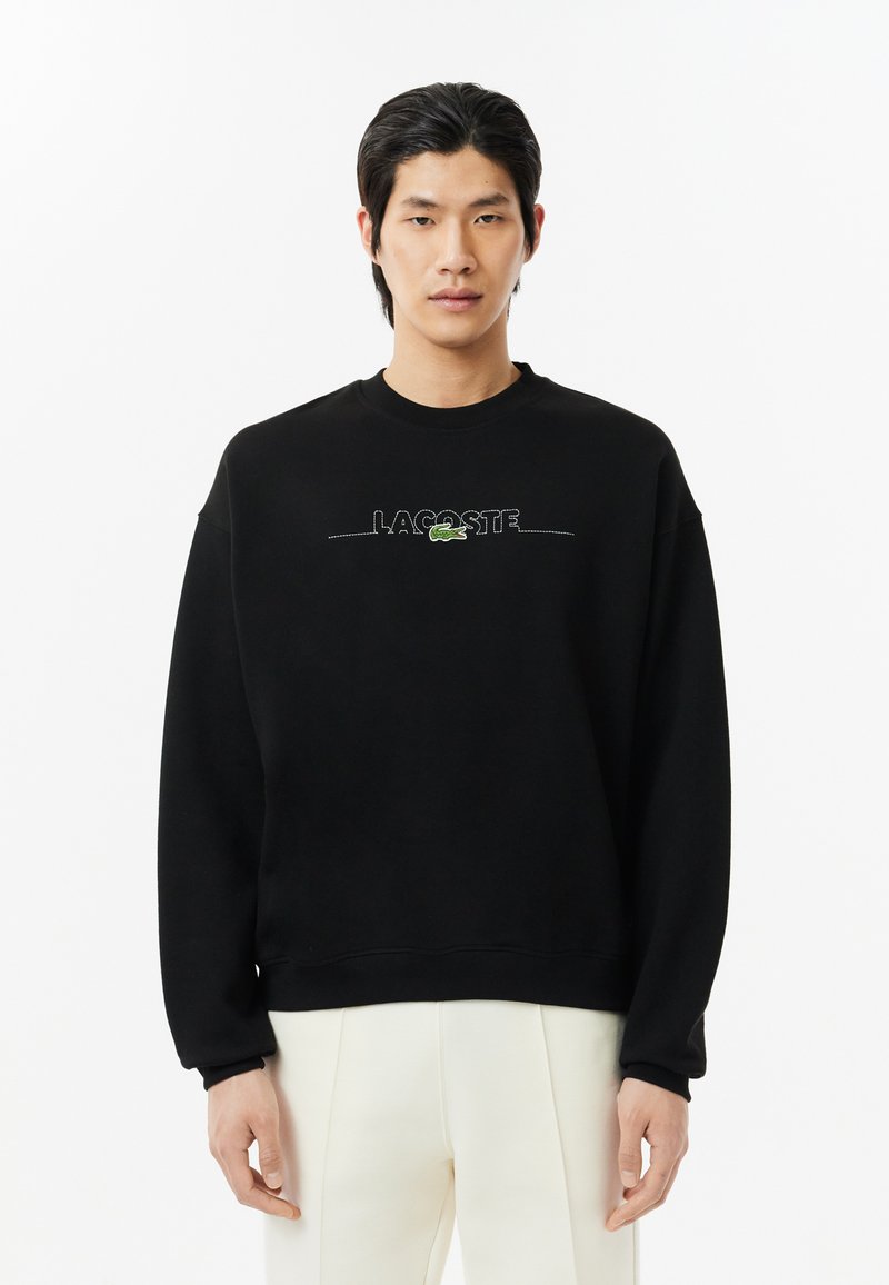 Sudadera negra hecha de mezcla de algodón, con cuello redondo, mangas largas y logo bordado 'LACOSTE' en verde en la parte frontal.