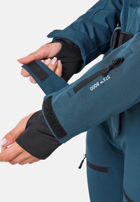 Wasserdichte Jacke mit einem teal-blauen Äußeren, schwarzen Bündchen mit Daumenlöchern, Klettverschlüssen und Reißverschlusstaschen für zusätzlichen Komfort.