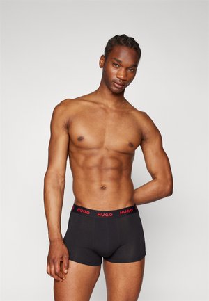 Boxer ajustados negros con un logo rojo de "HUGO" en la cinturilla, diseño ceñido, textura de tela suave y longitud a mitad del muslo.
