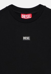 Μαύρο βαμβακερό μπλουζάκι με ριμπ γιακά, με έναν ορθογώνιο λευκό και μαύρο λογότυπο "DIESEL" κοντά στη λαιμόκοψη.