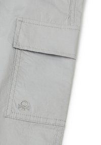 Světlé šedé cargo kalhoty s nakládací kapsou, viditelným šitím a výšivkou loga. Vyrobené z hladké, odolné tkaniny.