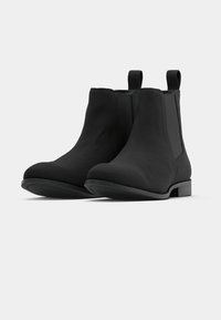 Botas negras hasta el tobillo con una textura lisa y mate, paneles laterales elásticos y tiradores. Punta redondeada y tacón bajo cuadrado. Suela de goma plana.